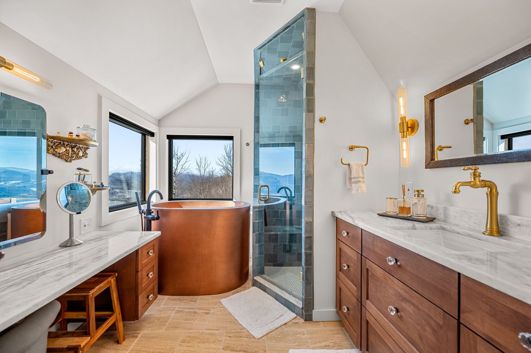 Hammered copper soaking tub, blue tiled shower, and marble vanities with mountain views