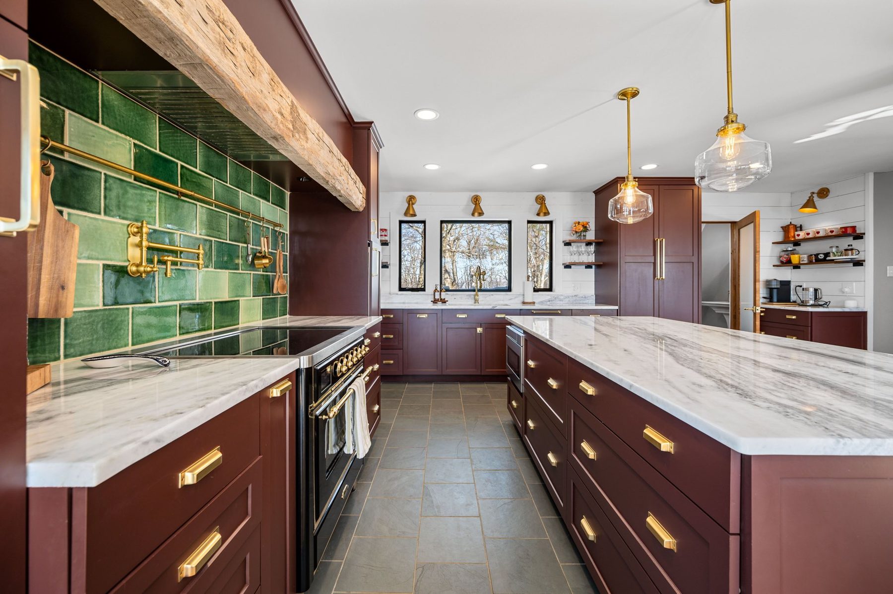 Burgundy cabinetry, emerald subway tile, marble island, and brass pendants