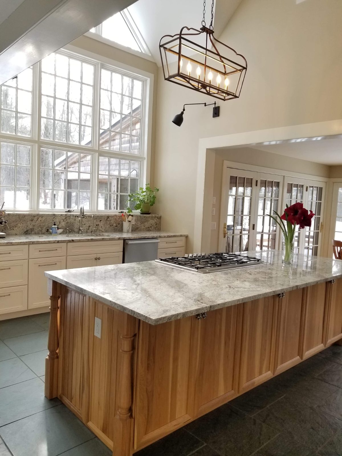 Hickory kitchen island with granite top and cream perimeter cabinetry under vaulted windows