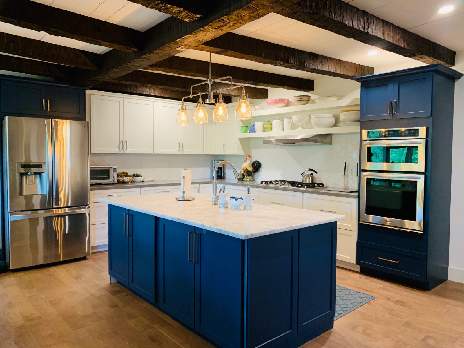 Navy island and white cabinetry with rustic beams and marble counters