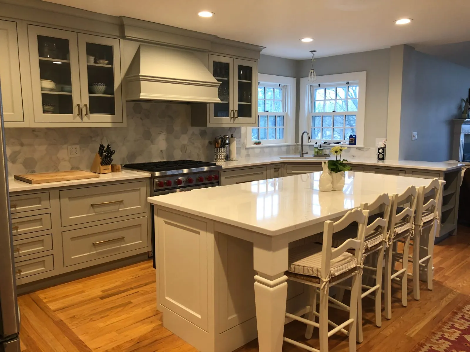 Gray-green inset cabinetry with brass hardware, hexagon marble backsplash, and Wolf range