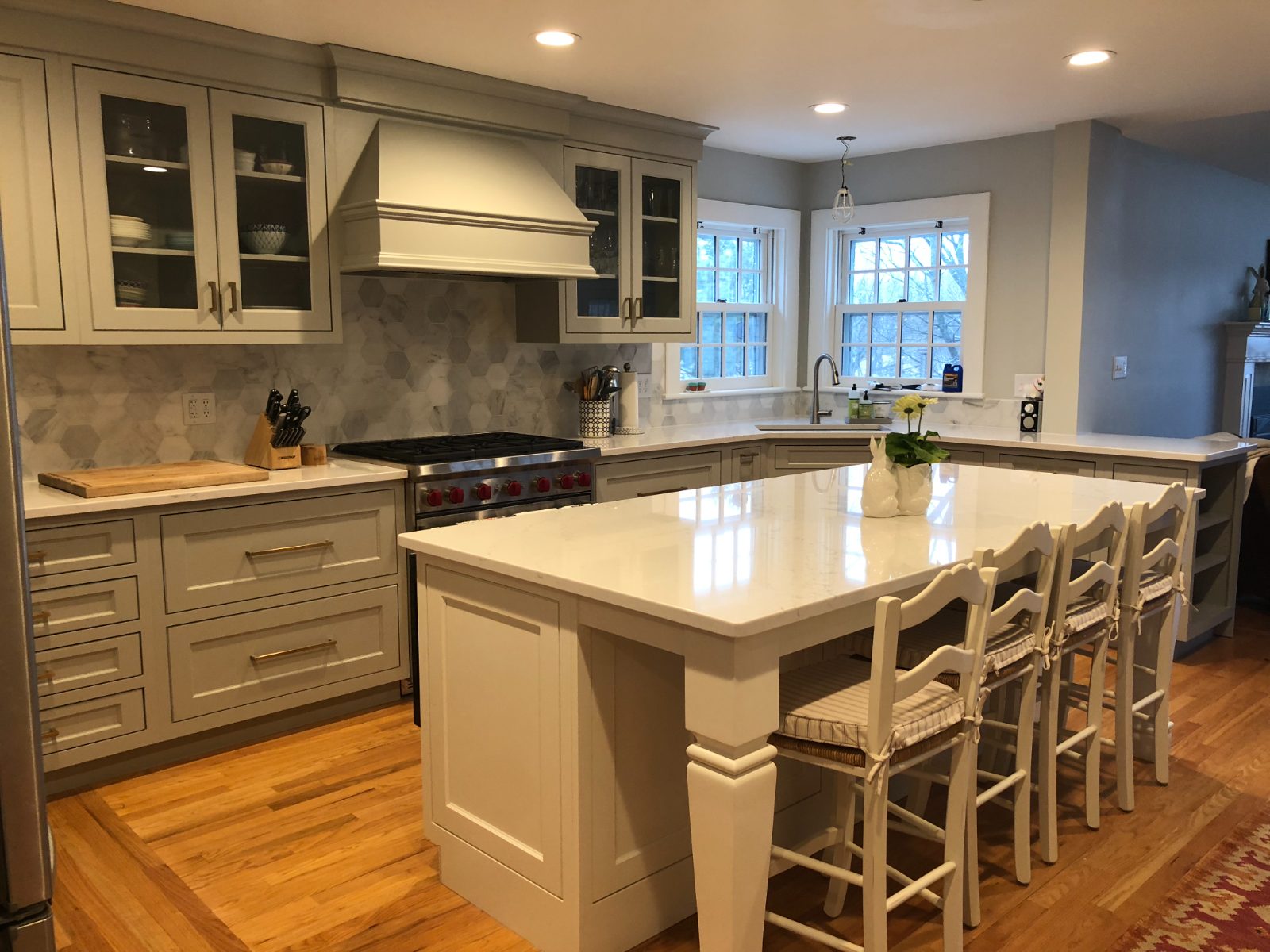 Gray-green inset cabinetry with brass hardware, hexagon marble backsplash, and Wolf range